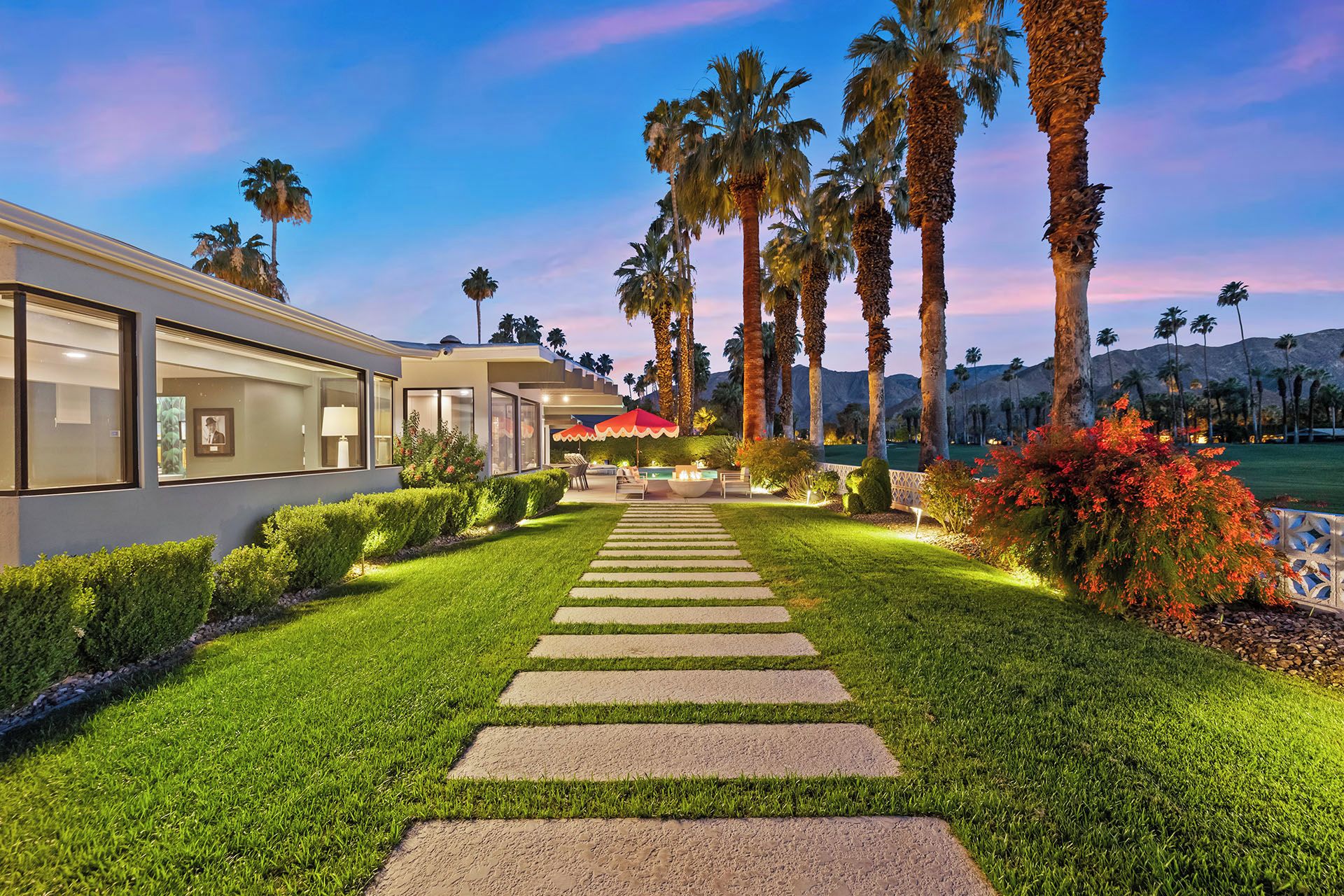 A well-maintained garden pathway leading to a modern building with large windows and a patio area.