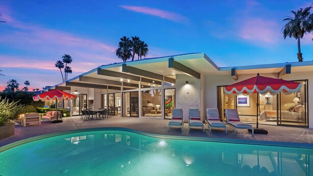 Ein modernes Haus mit Swimmingpool, Sitzgelegenheiten im Freien und Palmen.