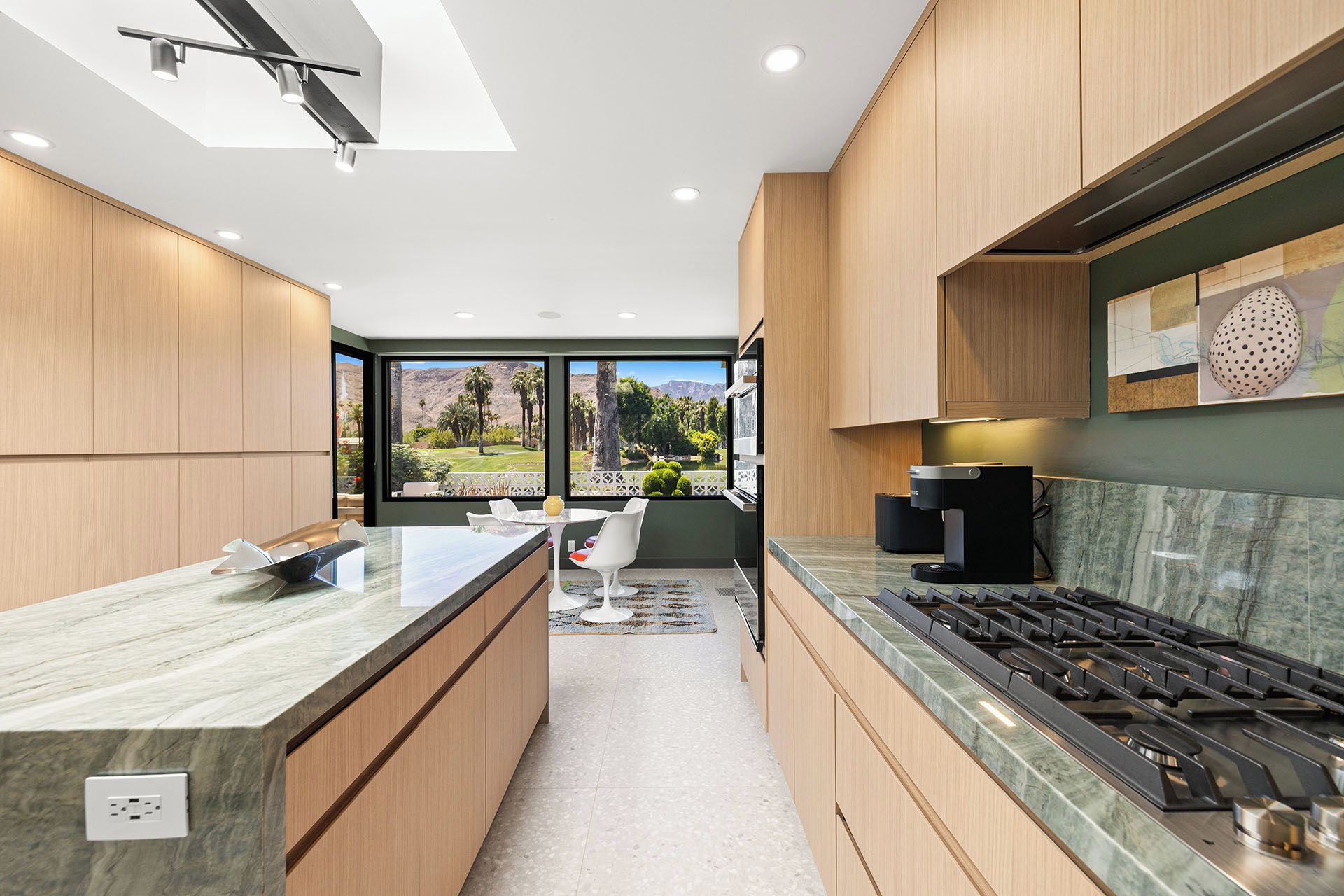 A modern kitchen with wooden cabinets, a marble countertop, a gas stove, and a view of a golf course through large windows.