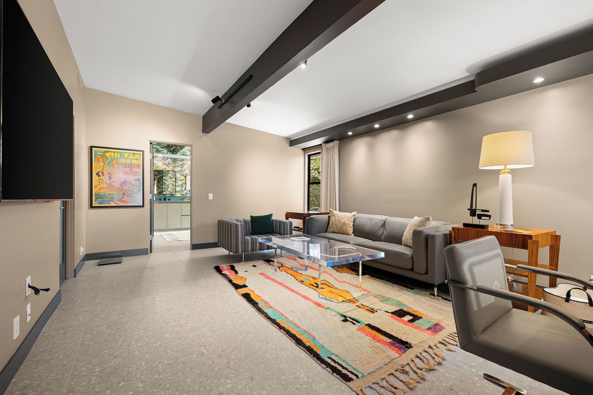 Un salon moderne avec un canapé, des fauteuils, une table basse en verre, un tapis coloré et une lampe.