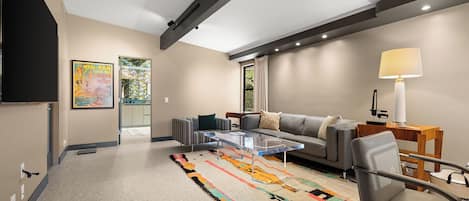 A modern living room with a sofa, armchairs, a glass coffee table, a colorful rug, and a lamp.