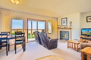 A living room with a fireplace, a television, and a view of the beach.