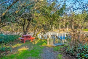 A picnic area with a bench and a small wooden deck by a body of water.