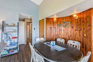 A dining area with a wooden wall, a round table, white chairs, and a bookshelf with books. - Hi-Tide Resort, Top Floor, Queen Bed, Unit 32 (Moclips)