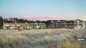 A coastal hotel with multiple-story buildings, a grassy foreground, and a forested background.