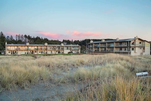 A coastal hotel with multiple-story buildings, a grassy foreground, and a forested background.