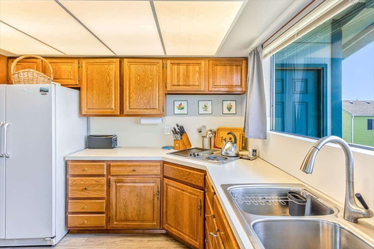 Una cocina con armarios de madera, un refrigerador blanco, un lavamanos y una ventana con vista a una casa.