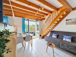 A modern interior with a dining area, sofa, staircase, and large windows. - Erdeven - 3-room house - 42m² - Wifi - 1* (ERDEVEN)