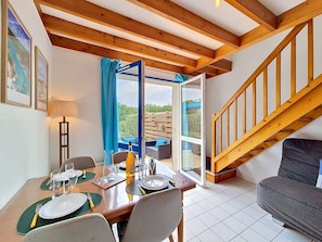 A dining area with a table set for four, a sofa, a staircase, and a view of the outdoors. - Erdeven - 3-room house - 42m² - Wifi - 1* (ERDEVEN)