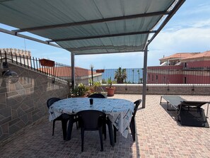 An outdoor patio with a covered table and chairs, potted plants, and a view of the sea. - Sea view terrace (Siracusa)