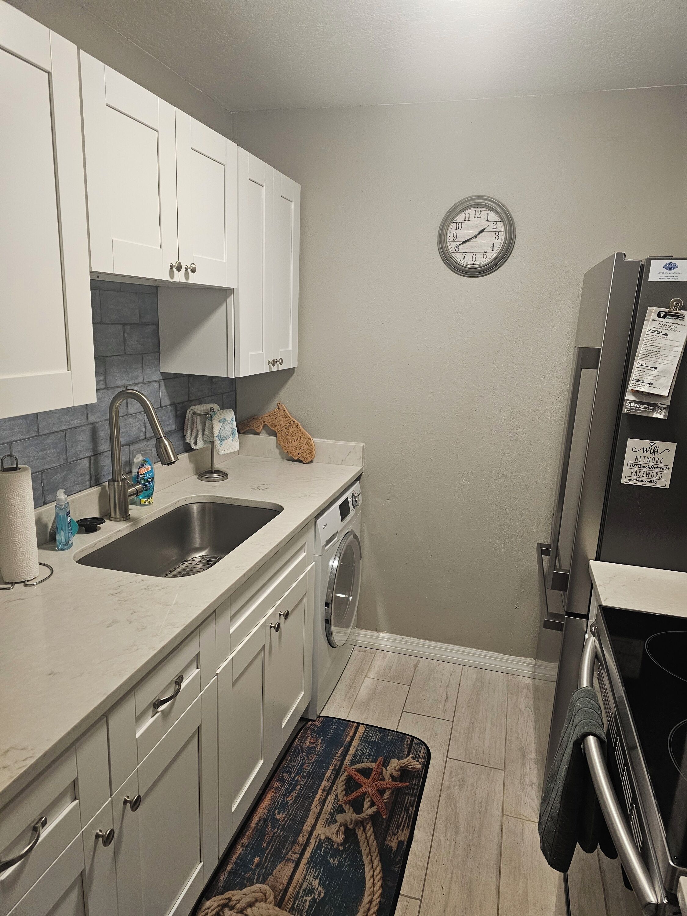 Cocina compacta con lavamanos, lavadora, reloj y refrigerador.