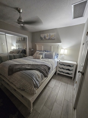 Ein Schlafzimmer mit einem Bett, einem Nachttisch, einem Spiegel und einem Deckenventilator.