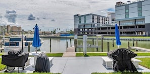 Blick auf das Wasser mit einem modernen Gebäude, einem Steg mit einem Boot und einer Terrasse mit Sonnenschirmen.