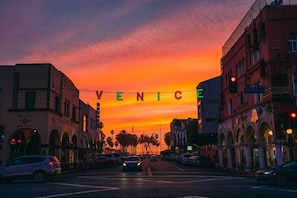 Ein Sonnenuntergang mit einer Straßenszenerie, wobei das Wort "VENICE" in Leuchtreklame geschrieben steht.