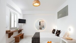 Ett modernt vardagsrum med en tv, en rund spegel, en soffa med kuddar, ett soffbord med frukt och en hängande lampa.