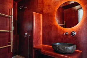 A bathroom with a round mirror, a sink, and a shower. - Lumera Sunrise Suite | Heated Jacuzzi & Sea View (Thira)
