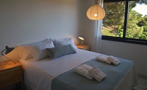 A neatly made bed with pillows, a bedside lamp, and towels on a wooden nightstand.