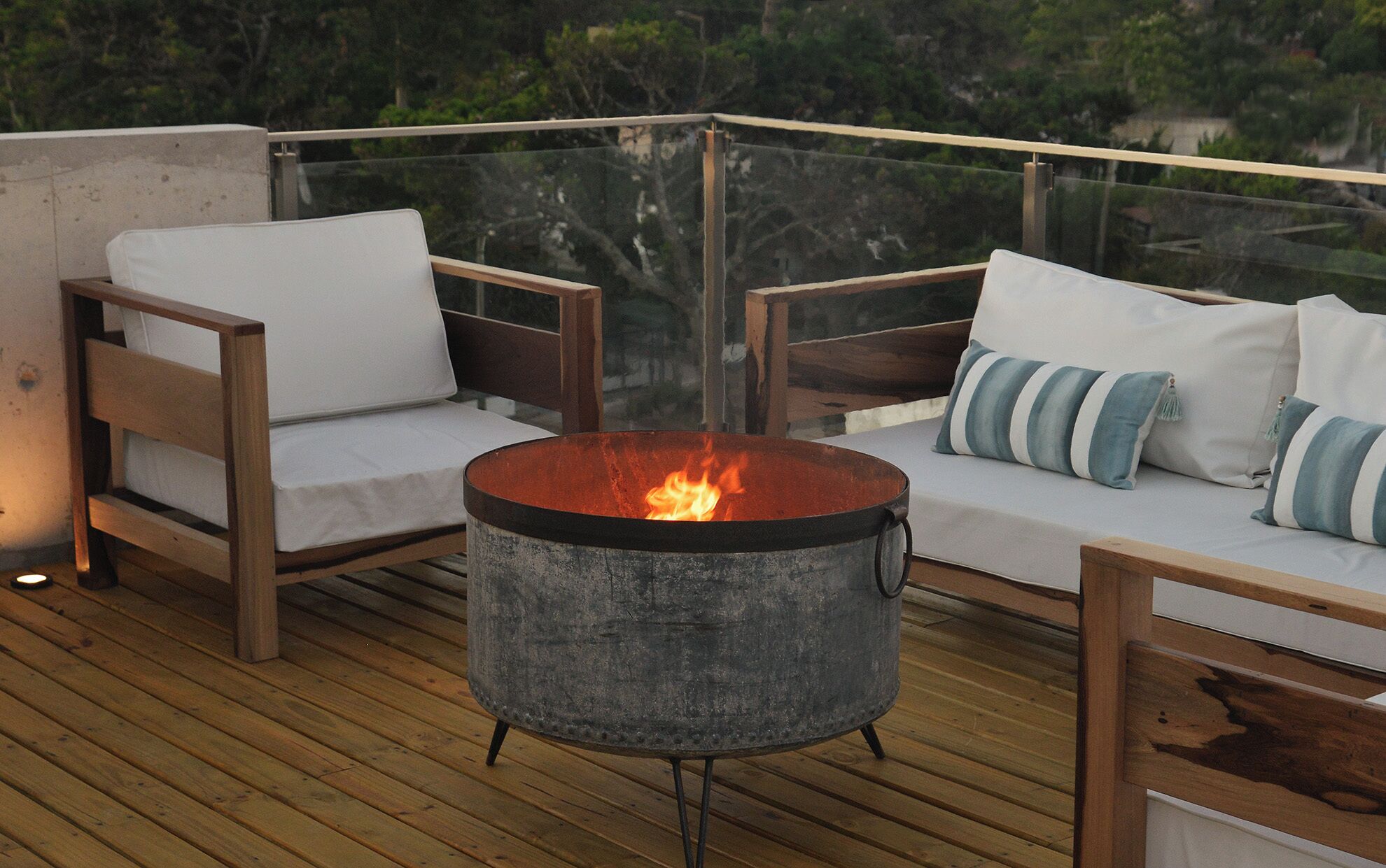 Una terraza con dos sillas de madera, una mesa redonda con fuego y un sofá con almohadones a rayas.