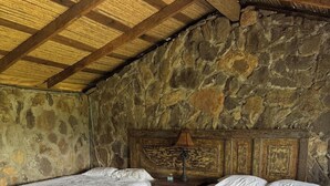 Een kamer met twee bedden, een stenen muur, een houten plafond en een betegelde vloer.
