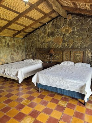 Una habitación con dos camas, una pared de piedra, techo de madera y suelo de baldosas.