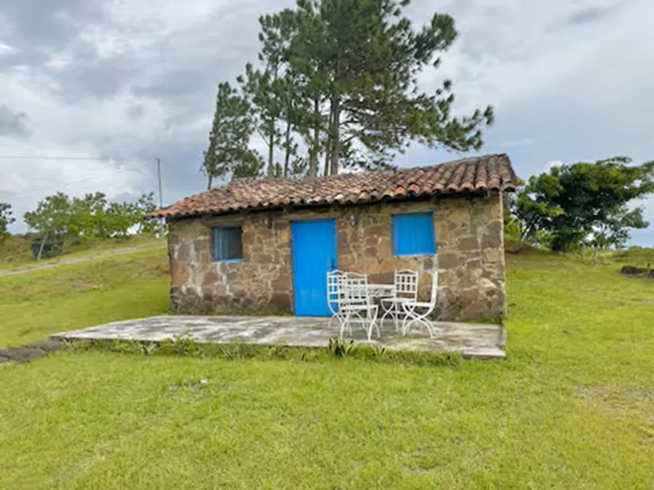 A stone building with a tiled roof, two blue doors, and a small outdoor seating area with metal chairs and a table.