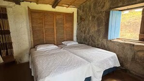 Une pièce avec un lit, une fenêtre et un mur en pierre.
