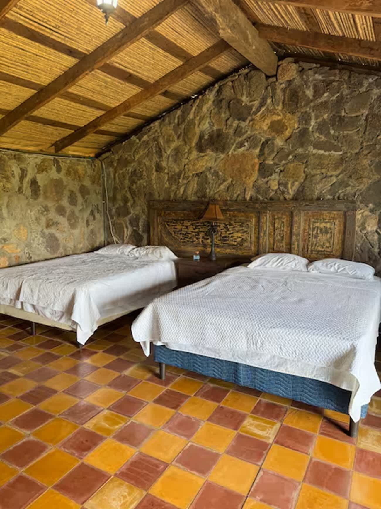 Une chambre avec deux lits, un mur en pierre et un sol carrelé.