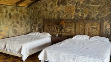 Une chambre avec deux lits, un mur en pierre et un sol carrelé.
