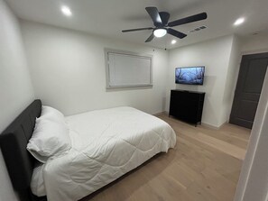 Un dormitorio con una cama, ventilador de techo, televisión y una puerta.