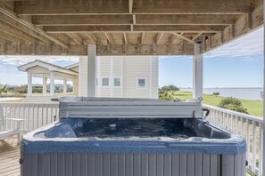 A hot tub under a wooden deck with a view of a building and a body of water. - 5590 - Sand Hills South, Soundfront 6BR, 4BA Nags Head retreat for 12. (Nags Head)