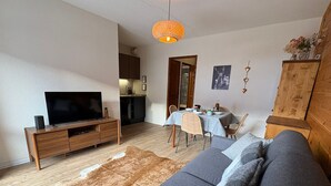 A living room with a sofa, TV, wooden cabinet, and a dining area with a table and chairs. - Comfortable studio with terrace and WIFI in Serre Chevalier (Serre Chevalier Chantemerle)