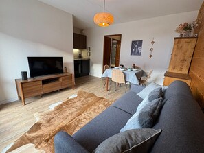 A living room with a sofa, TV, wooden cabinet, and a dining area with a table and chairs. - Comfortable studio with terrace and WIFI in Serre Chevalier (Serre Chevalier Chantemerle)