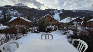 A wooden cabin with a snow-covered roof, surrounded by snow-covered ground and trees, with mountains in the background. - Comfortable studio with terrace and WIFI in Serre Chevalier (Serre Chevalier Chantemerle)
