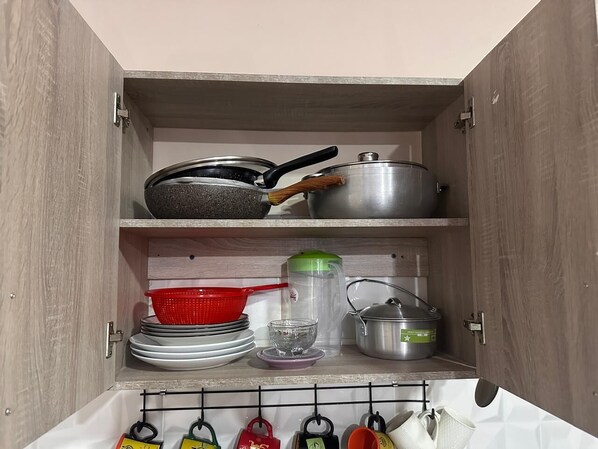 Un armario de cocina con repisas que contienen utensilios de cocina, platos y un perchero con cubiertos.
