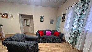 Una habitación con un sofá de color oscuro, una silla, una puerta y una cortina con estampado floral.