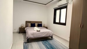 A bedroom with a bed, bedside tables, a wardrobe, a window, and a ceiling light. - Couramina (Dakar)