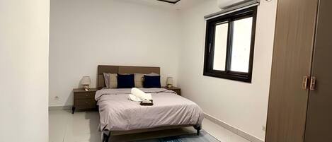 Une chambre à coucher comprenant un lit, des tables de chevet, une armoire, une fenêtre et un luminaire au plafond.