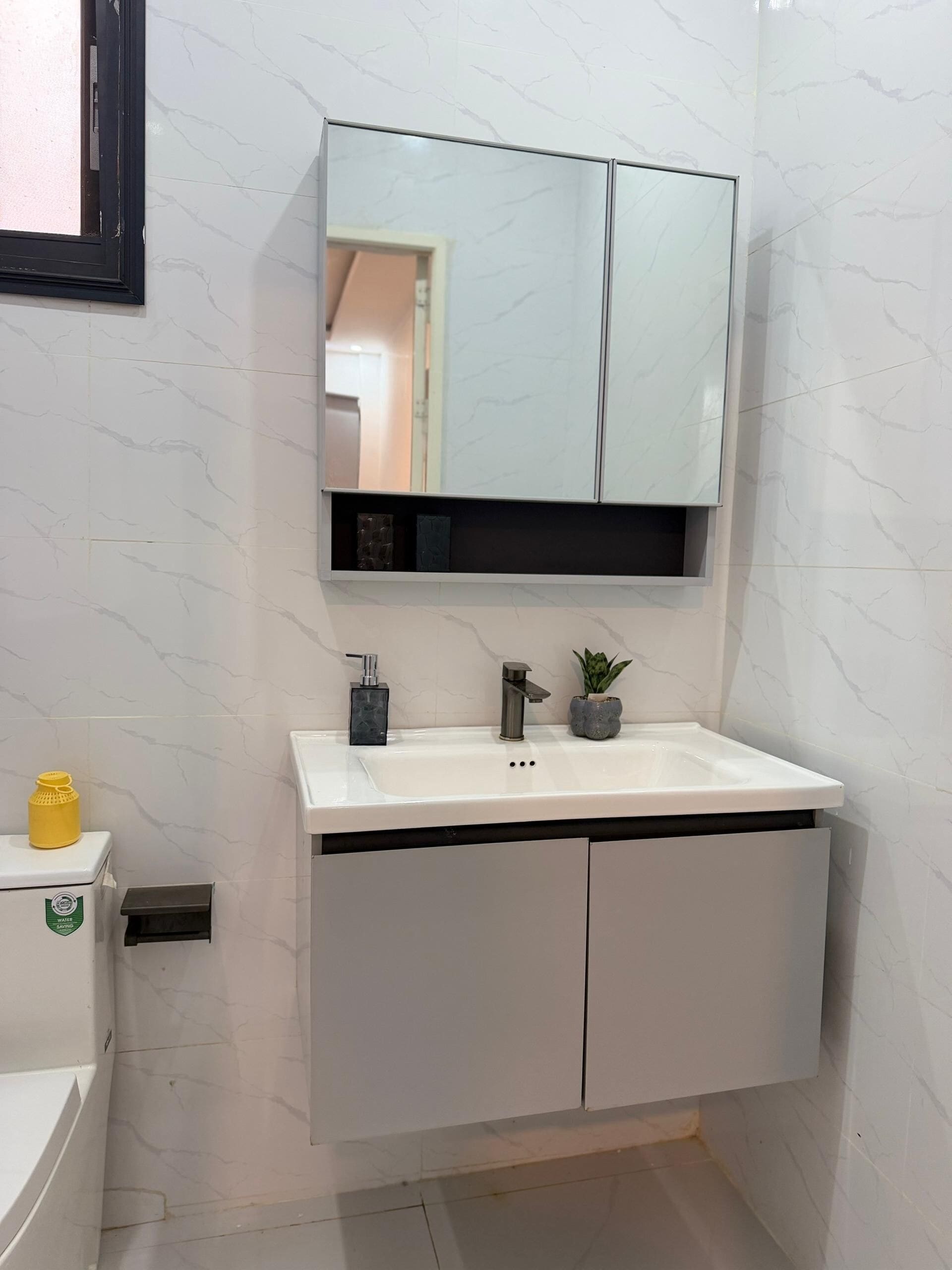 Ein Badezimmer mit einem weißen Waschbecken, einem Spiegel darüber und einem kleinen Topfpflanzen auf der Ablagefläche.
