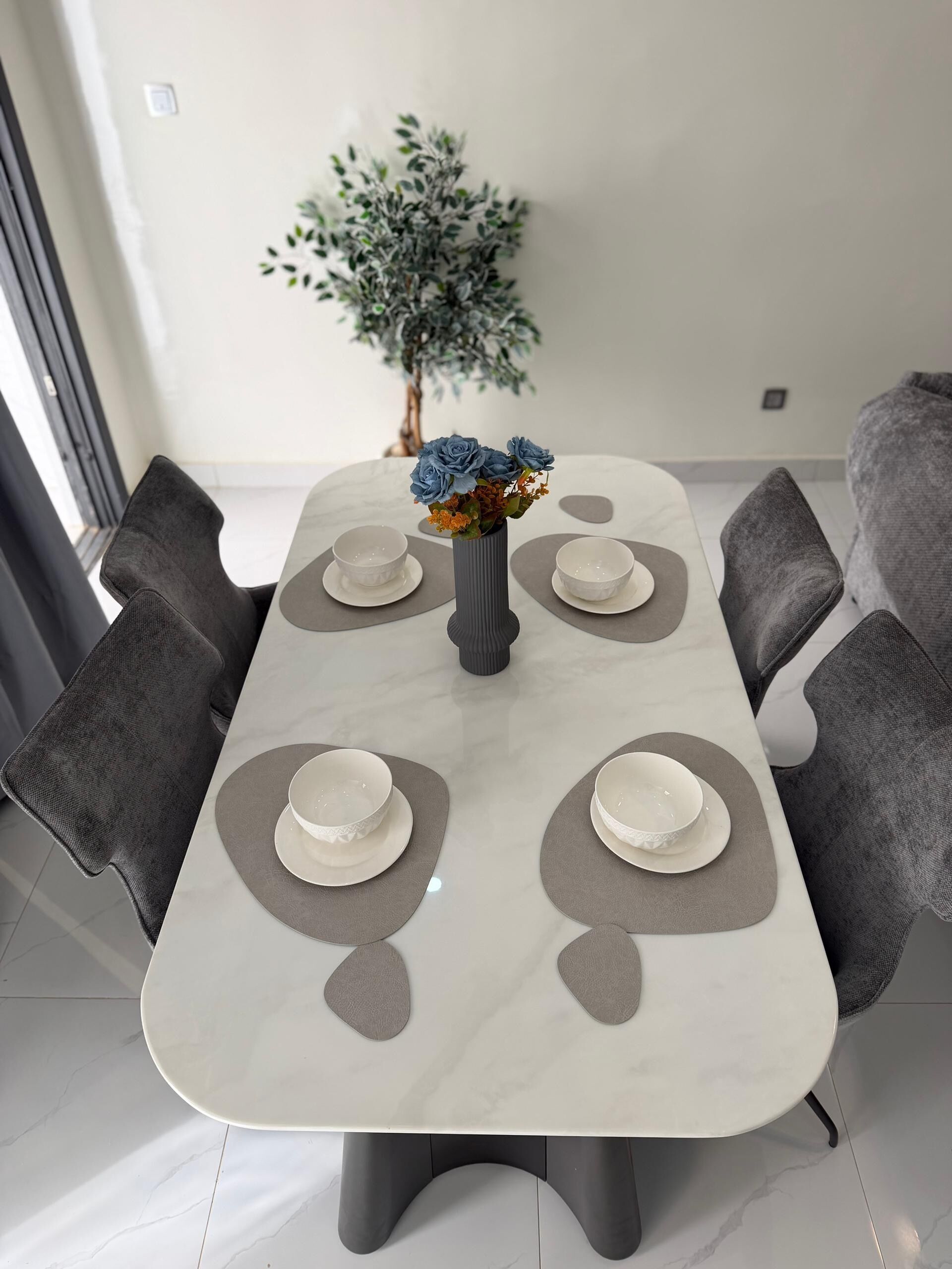 Una mesa de comedor con cuatro sillas, un jarrón con flores y una planta al fondo.
