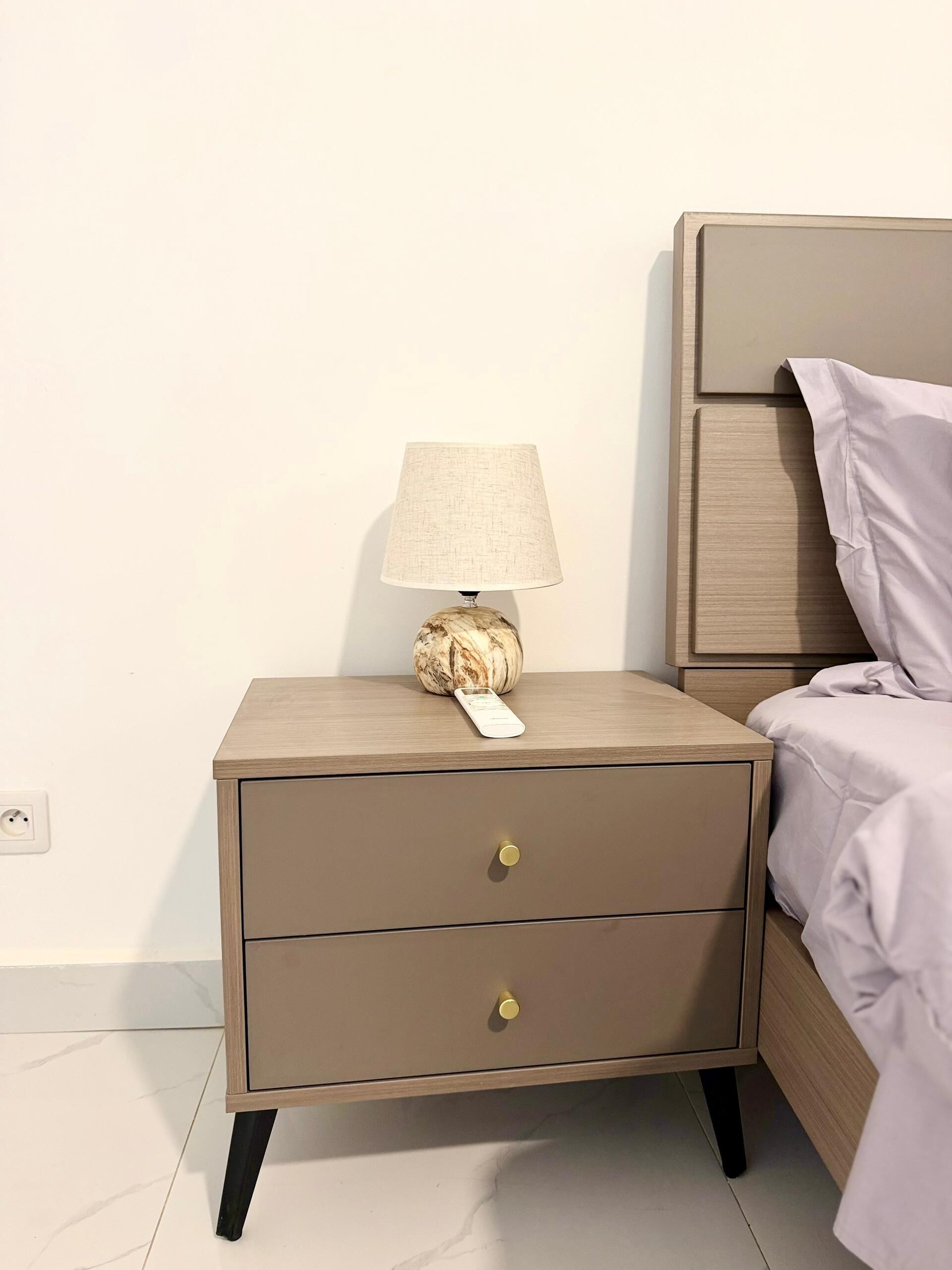 A bedside table with a lamp, a power outlet, and a drawer.