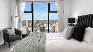 Ein Hotelzimmer mit großem Fenster, einem Bett, einem Sessel und einer Stehlampe.