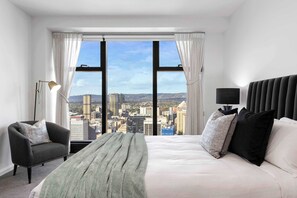 A hotel room with a large window, a bed, a chair, and a floor lamp. - Luminesque Skyhome | Executive Residence in Adelaide CBD (Adelaide)
