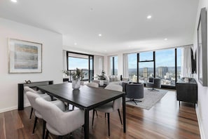 A modern living room with a dining area, large windows, and a city view. - Luminesque Skyhome | Executive Residence in Adelaide CBD (Adelaide)