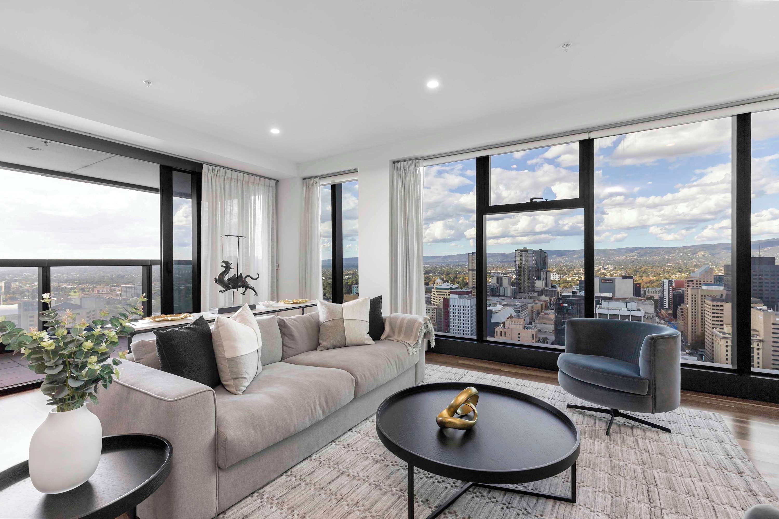 A modern living room with a large window, a sofa, a coffee table, and a chair.