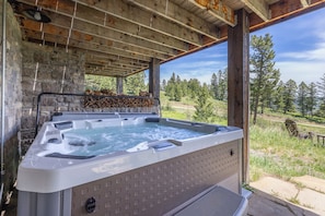 Un bain à remous avec un mur en pierre en arrière-plan, un plafond en bois et une vue sur une forêt.