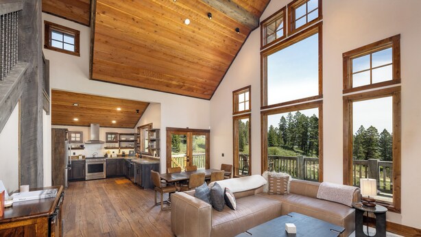 A spacious living area with a high ceiling, large windows, a kitchen, and a view of the outdoors.