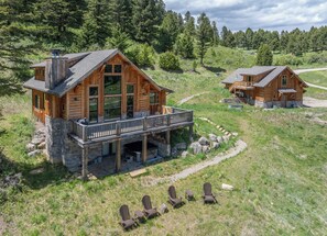Une cabane en bois dotée d’un balcon, construite sur des fondations en pierre, et entourée d’une pelouse où sont disposées des chaises Adirondack.