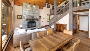 A spacious living area with a stone fireplace, wooden ceiling, and a large dining table.