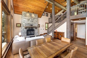 Amplia sala de estar con chimenea de piedra, techo de madera y una gran mesa de comedor.