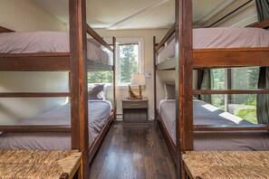A bunk bed room with a window, a bedside table, and a lamp.